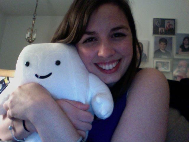 Image is a selfie of me smiling at the camera. I'm holding a stuffed adipose which looks like a marshmellow with two eyes, a smile, and one white tooth in its mouth. 
