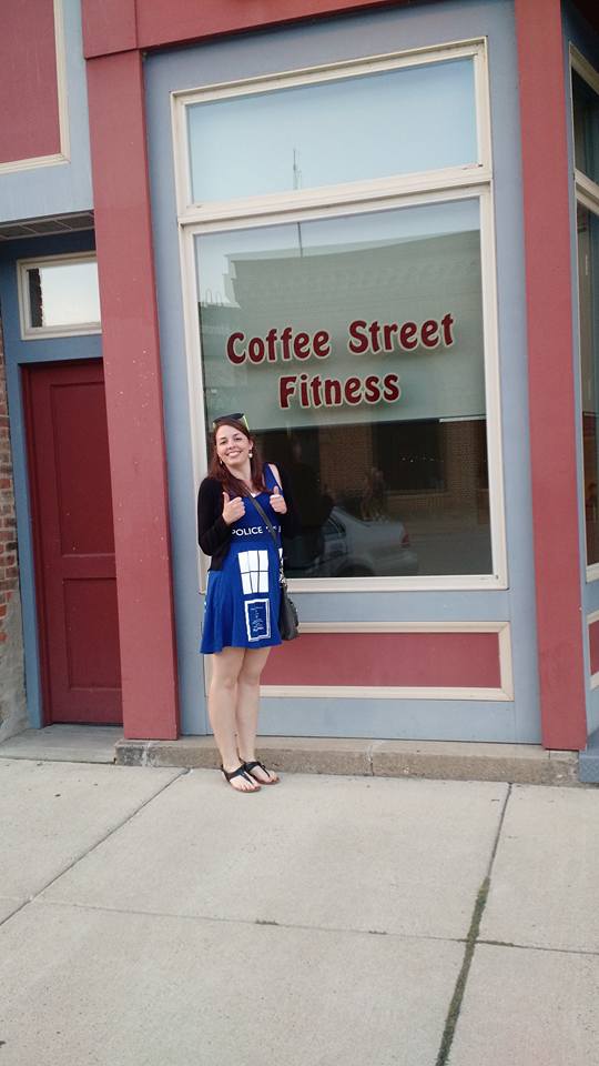 [Image is a picture of a woman standing outside of a building that says "Coffee Street Fitness" She's wearing a Tardis dress and is in sandals.]