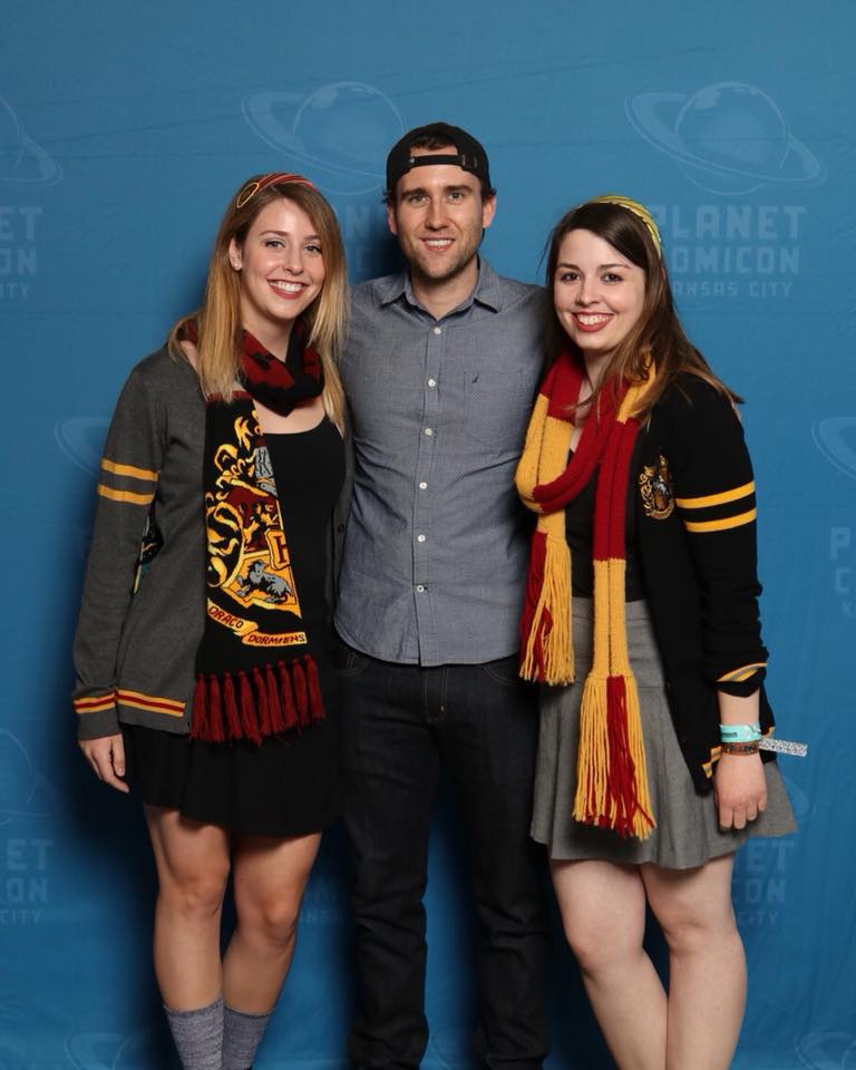 [Image is of three people standing behind a Planet Comicon  background. The two women are on either side of Matthew Lewis. We are both wearing Gryffindor  Hogwarts clothing]