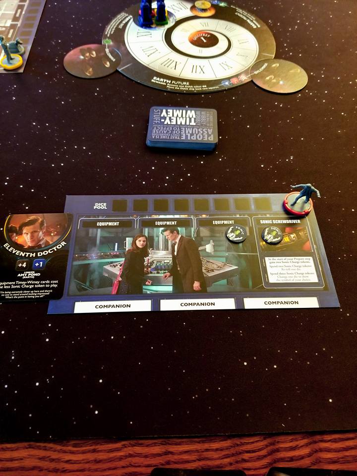 Image shows a game card for the game, Doctor Who: Time of the Daleks. It shows the eleventh doctor and Clara. There are three spots for companion cards. There's a figurine off to the right of the eleventh doctor. 