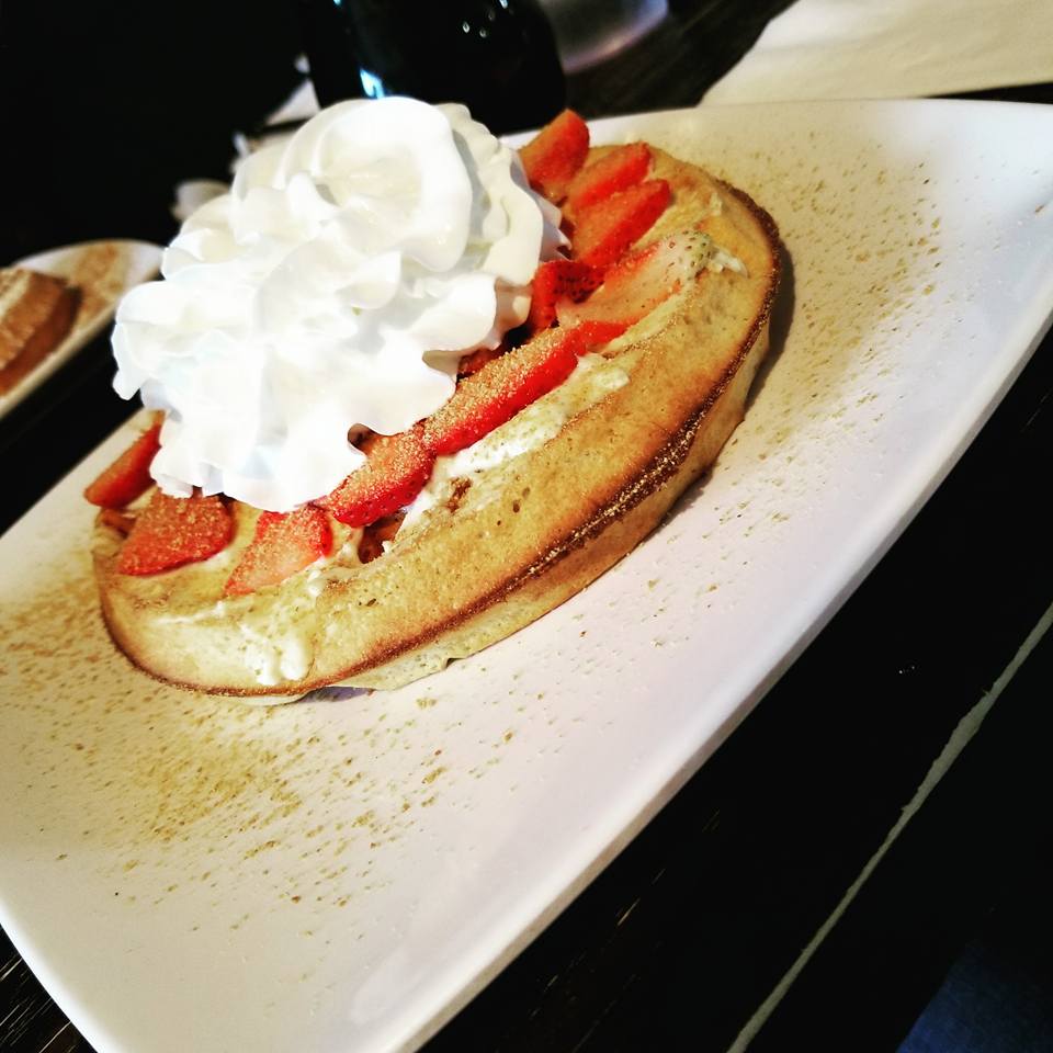 [Image shows a plate. On the plate is a belgian waffle with strawberries and whipped cream]