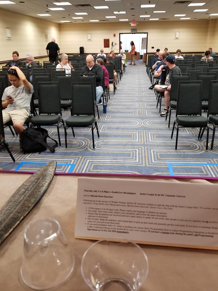 [Image shows a conference room with many rows of chairs. There are 19 people seated in chairs throughout the rows. The room feels pretty empty for how big it is]