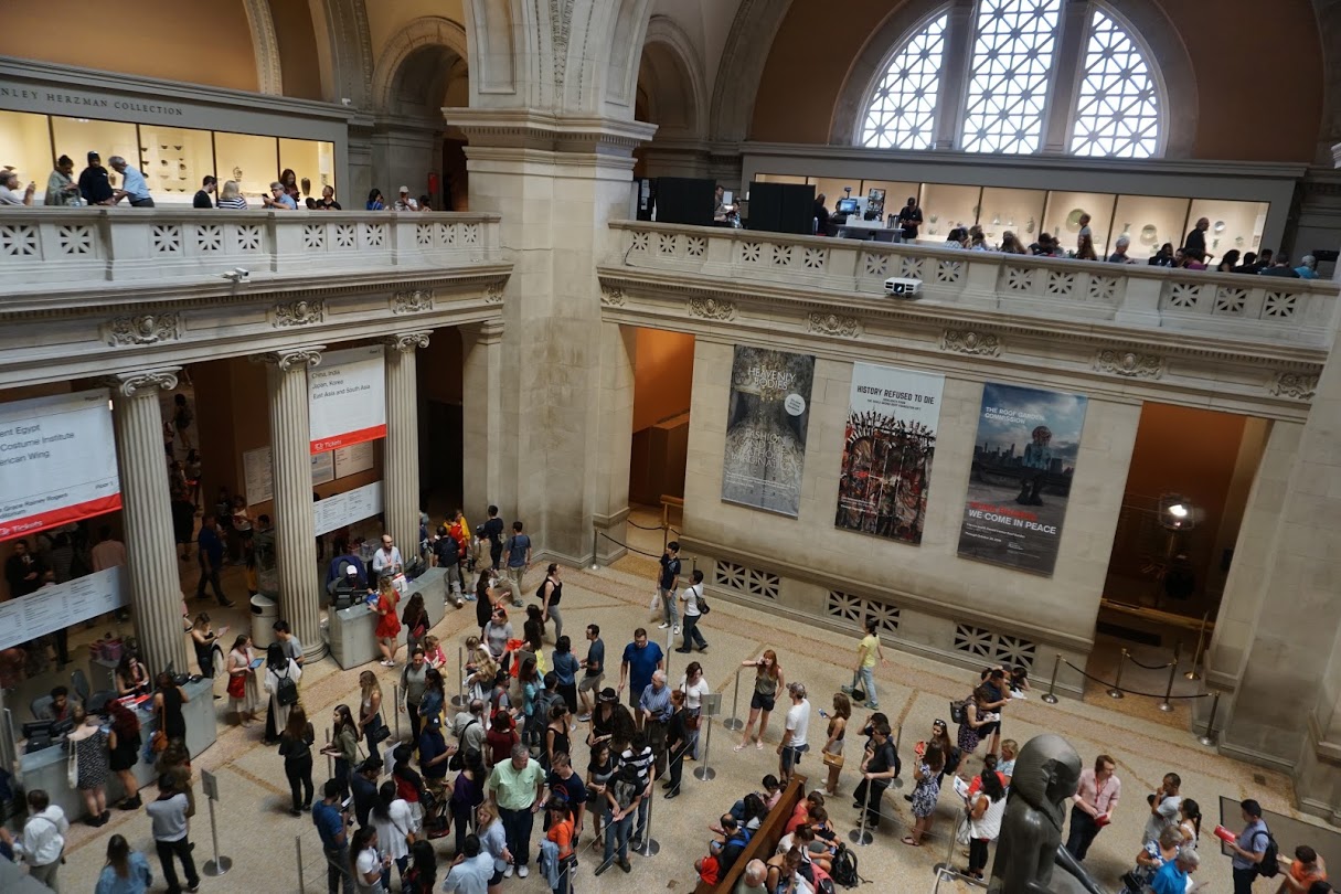[Image was taken from the 2nd floor of The Met. It shows people waiting in line below to access the museum with huge white pillars holding the floors together]