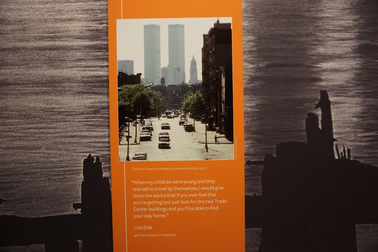 [Image is a picture of a description at the exhibit. The picture is dated and it shows the twin towers and a street with cars driving on it. There is text it reads "When my children were young and they started to travel by themselves, I would give them the advice that if you ever feel that you're getting lost just look for the two Trade Center buildings and you'll be able to find your way home" quote by Lois Eida Battery City Resident"