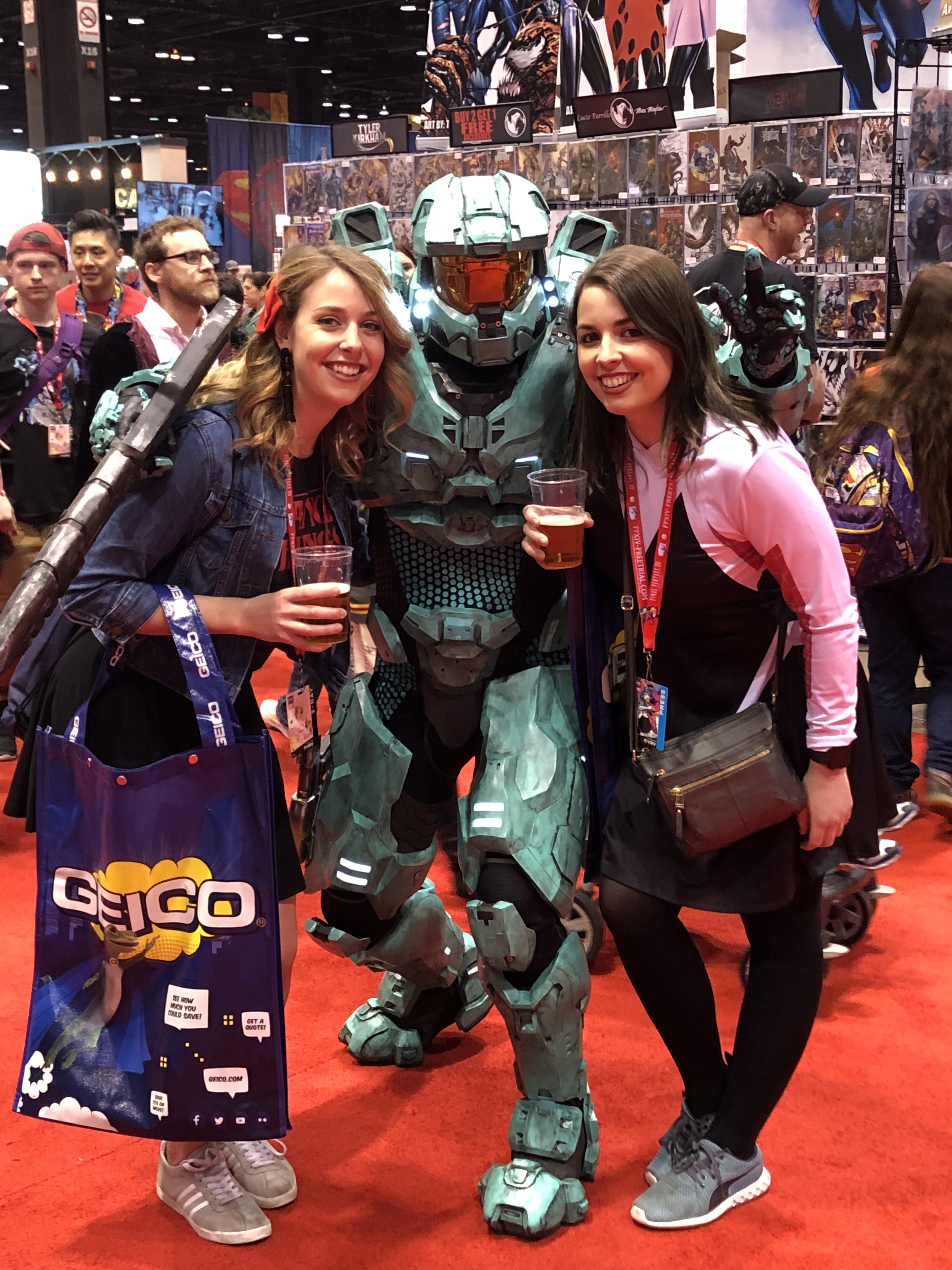 Image is a photo of my friend on the left and me on the right. In the midle is Master Chief from Halo 3. We are holding beers in our hands and smiling to the camera. 