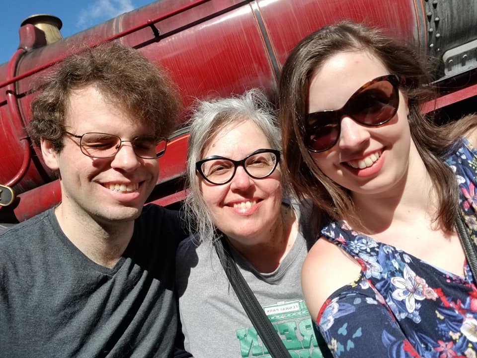 Image is a photo of my brother, my mom, and me looking at the camera and smiling. We were at Universal Studios in Orlando