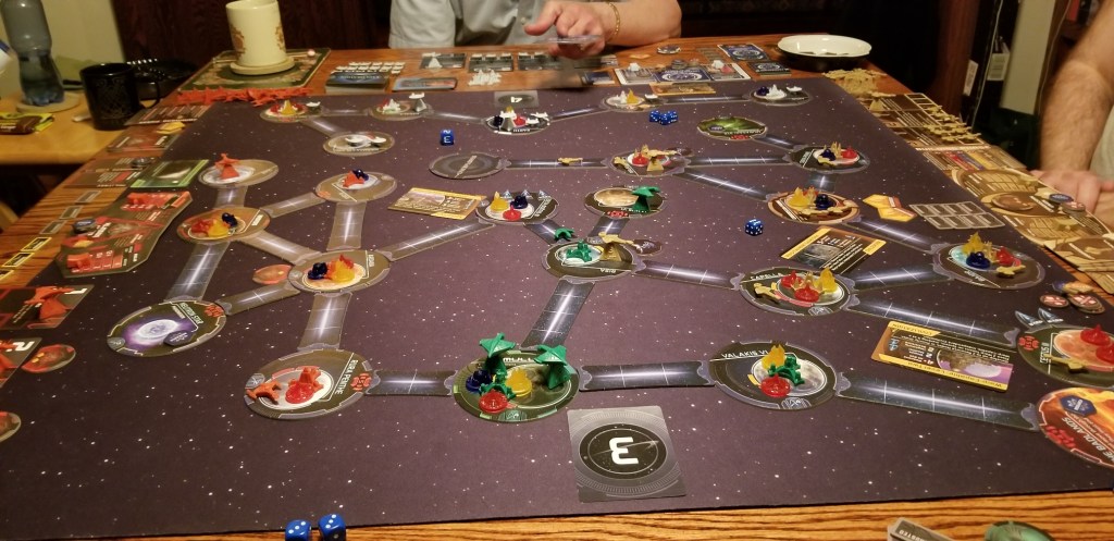 Image is a photo of a board game. There are circles with various game pieces on them. Connecting each circle is a white line that looks like space travel. There is a maze of circles, game pieces, and white light connecting everything together. 