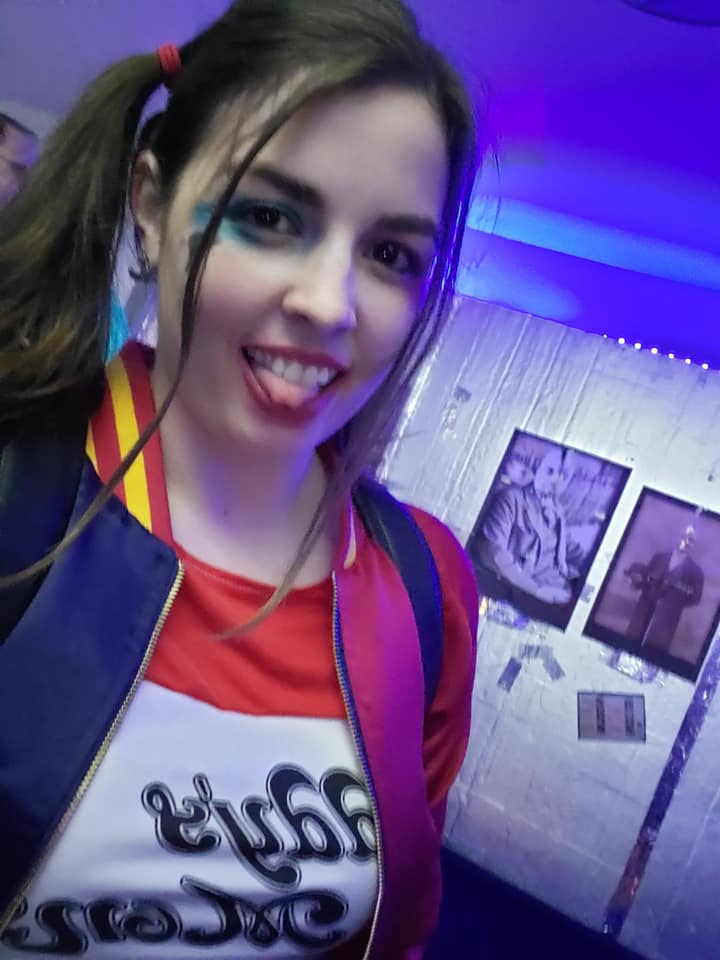 Image is a photo of me in my Harley Quinn cosplay. I have blue and red makeup on and I'm wearing a crop top that says "Daddy's Little Monster" on it. 