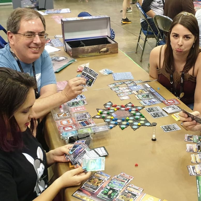 Image is a photo of 3 people. We are all playing a game. The winner is showing off his cards and how he won. 