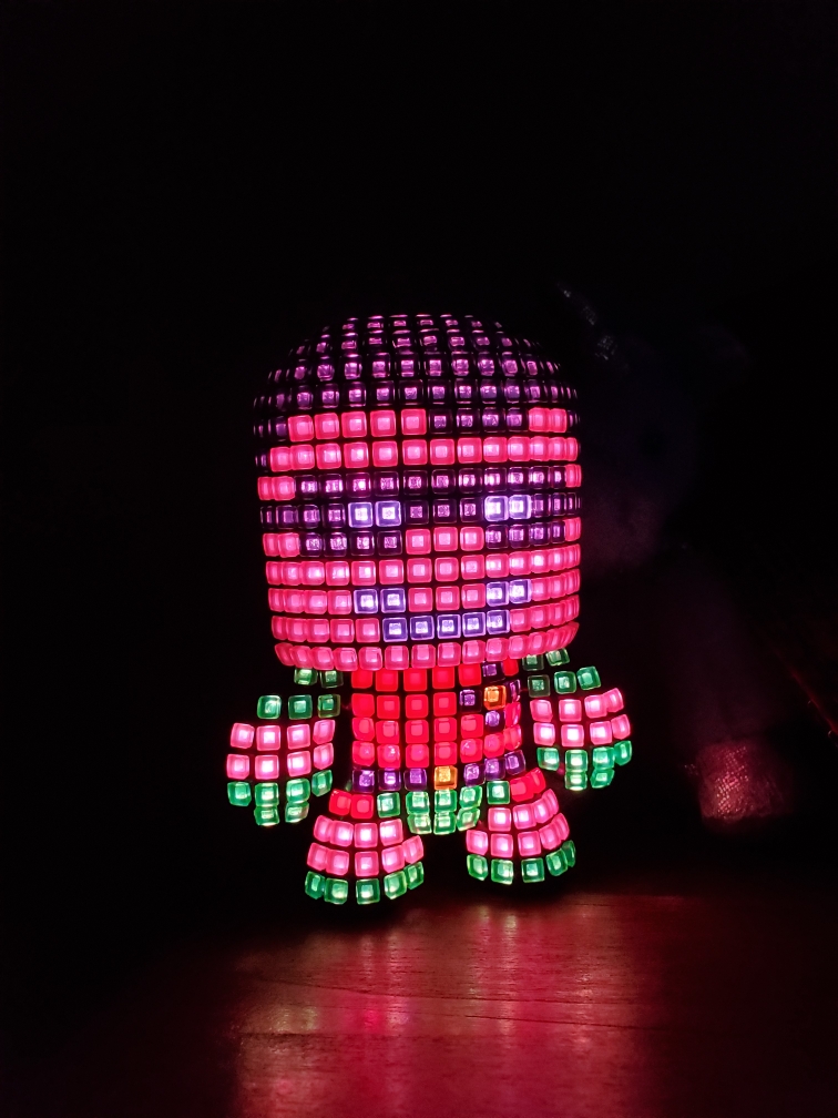 Image is a photo of Robin all lite up in the dark. It shows the different colors (red, green, yellow, white, beige, and black) and it actually looks like Robin. 