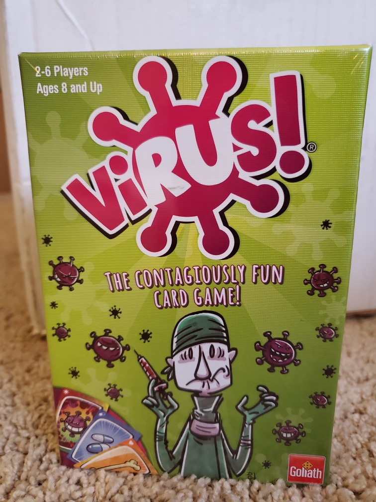 Image is a photo of the game, Virus. The wording of Virus is on a virus type molecule. On the cover of the game is a doctor wearing medical gear. He's holding a syringe and he looks concerned. There are several virus like molecule with eyes and mouths and they look menacing. 