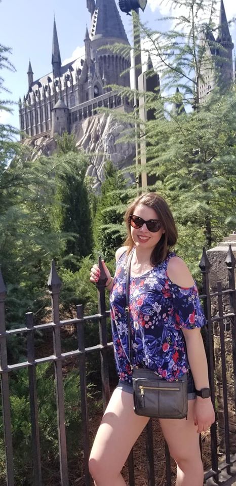 Image is a photo of me smiling at the camera. Behind me is Hogwarts at Universal Studios in Orlando. 