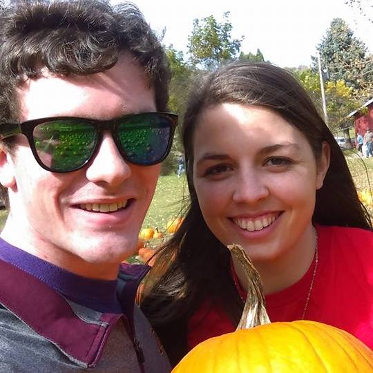 Image is a photo of me and my husband at an Apple Orchard. We are holding a pumpkin and smiling for the camera. 