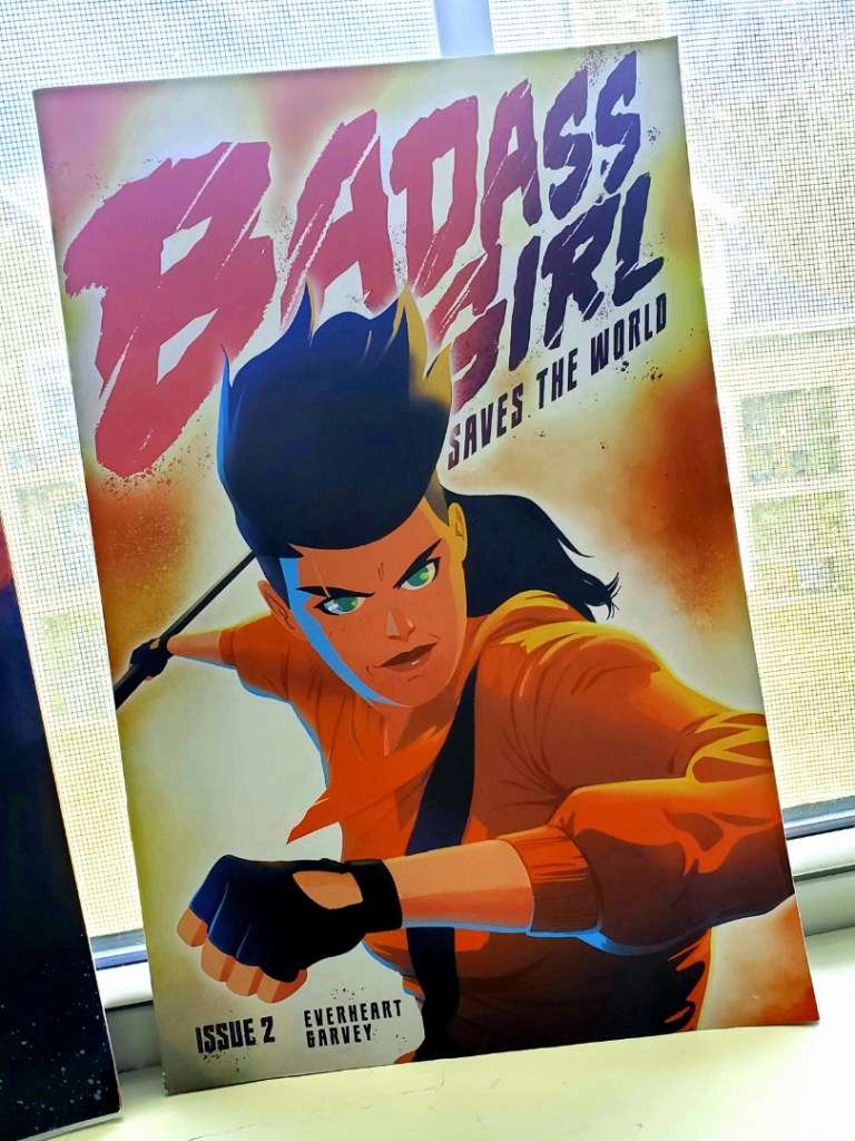 Image is a photo of a comic book called Badass Girl. It's a woman looking like she's attacking. She has black gloves and a spear in her right hand. 