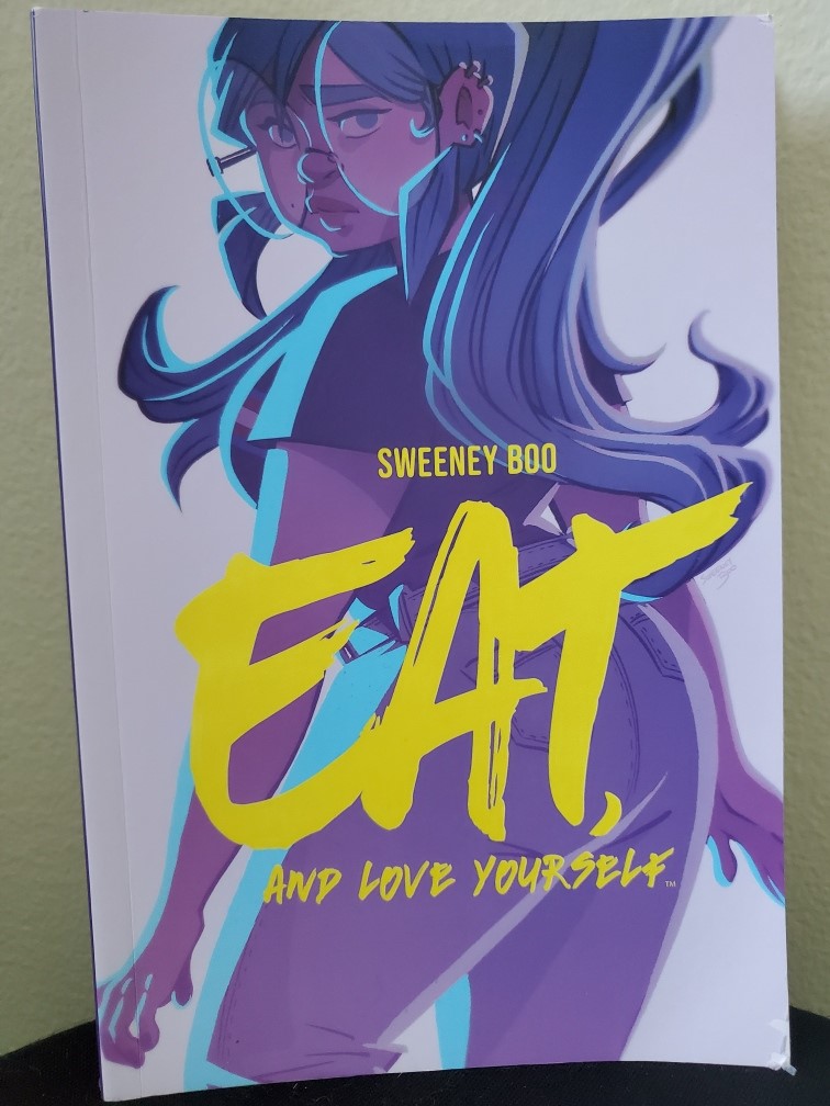 Image is a photo of a graphic novel titled Eat and Love Yourself by Sweeney Boo. It shows a woman with glasses looking off to the side. 