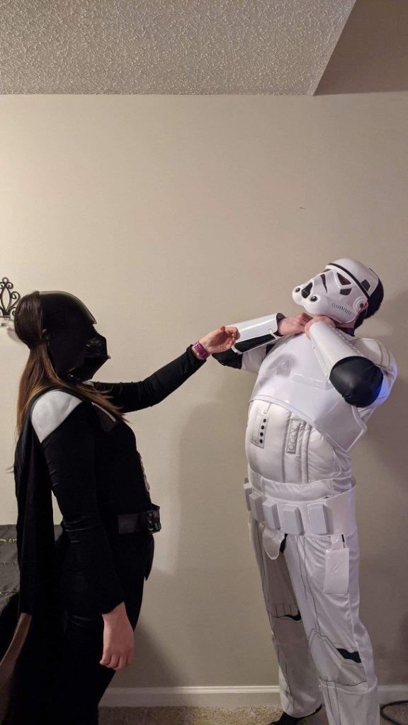 Image is a photo of me my fiance. We are dressed as Darth Vader and a Stormtrooper. I'm Darth Vader and I have my hand out and my fiance is clutching his throat. 
