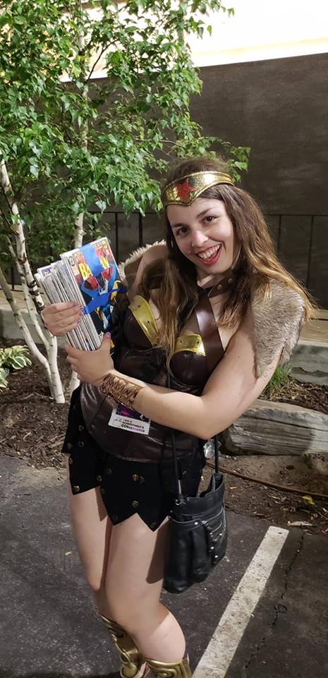 Image is a photo of me in a Wonder Womans Viking inspired cosplay. I'm holding a huge stack of comics in my hands. 