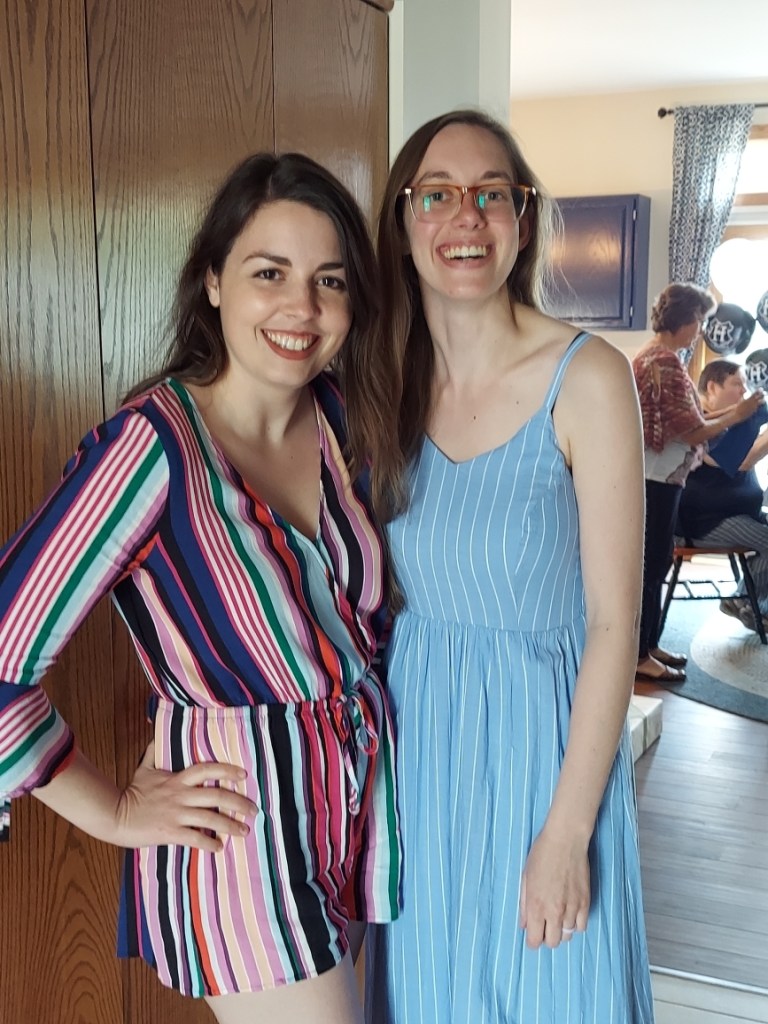 Image is a photo of me and my friend. We are smiling at the camera. I'm wearing a rainbow colored, vertical striped romper. She's wearing a blue and white vertical lined dress. 