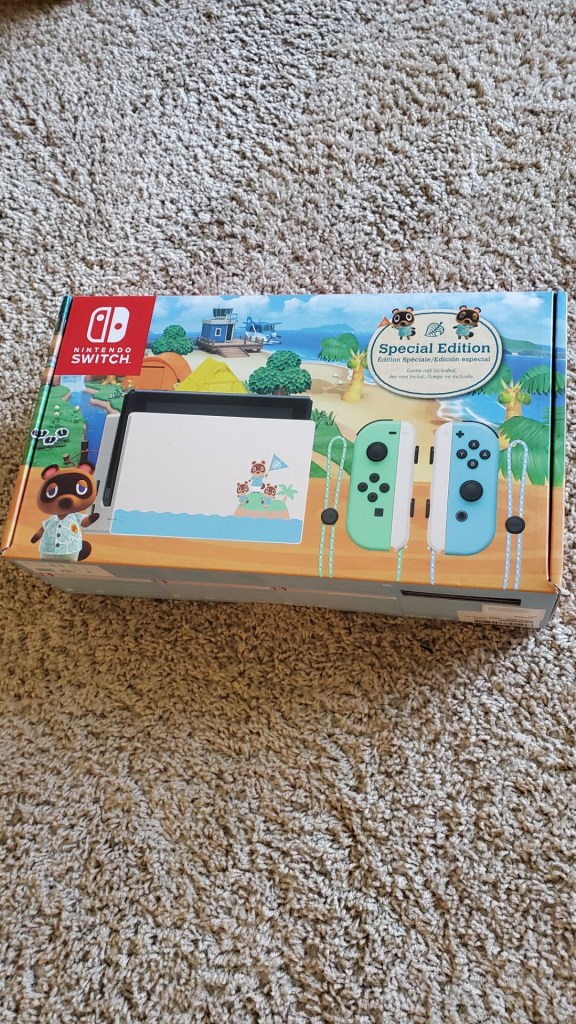 Image is a photo of the Animal Crossing: New Horizons Nintendo Switch special edition. It shows a bright green and bright blue controllers that attach to the Switch. It shows the Animal Crossing island in the background. 