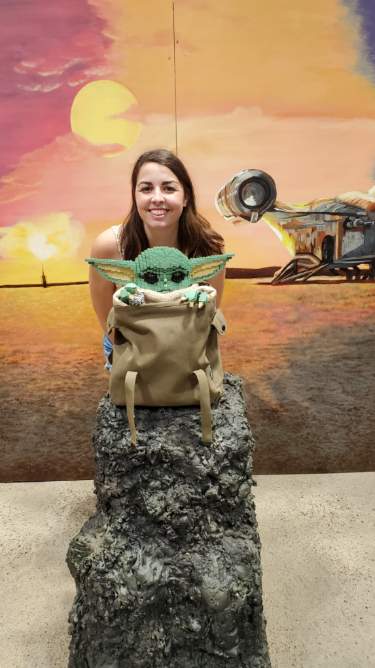 Image is a photo of me smiling. The background image is of Tattoine from Star Wars. In front of me is a LEGO Grogu from The Mandalorian. 
