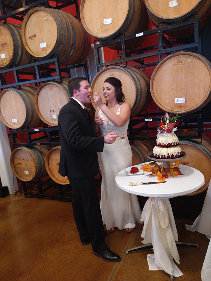 Image is a photo of me and my husband having first bites of our cake. I'm holding a fork and he's taking a bite of cake. 