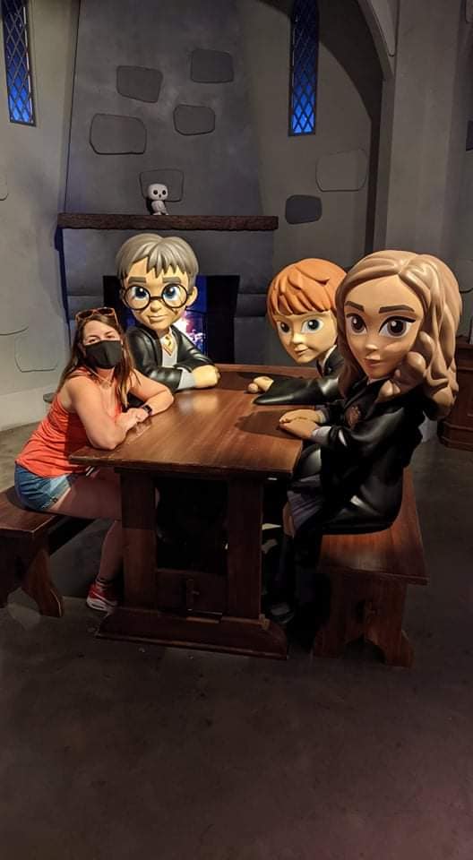 Image is a photo of me with a mask sitting at a table. There are three FUNKO figures of Harry Potter, Ron Weasley and Hermione Granger. I'm sitting next to Harry. 