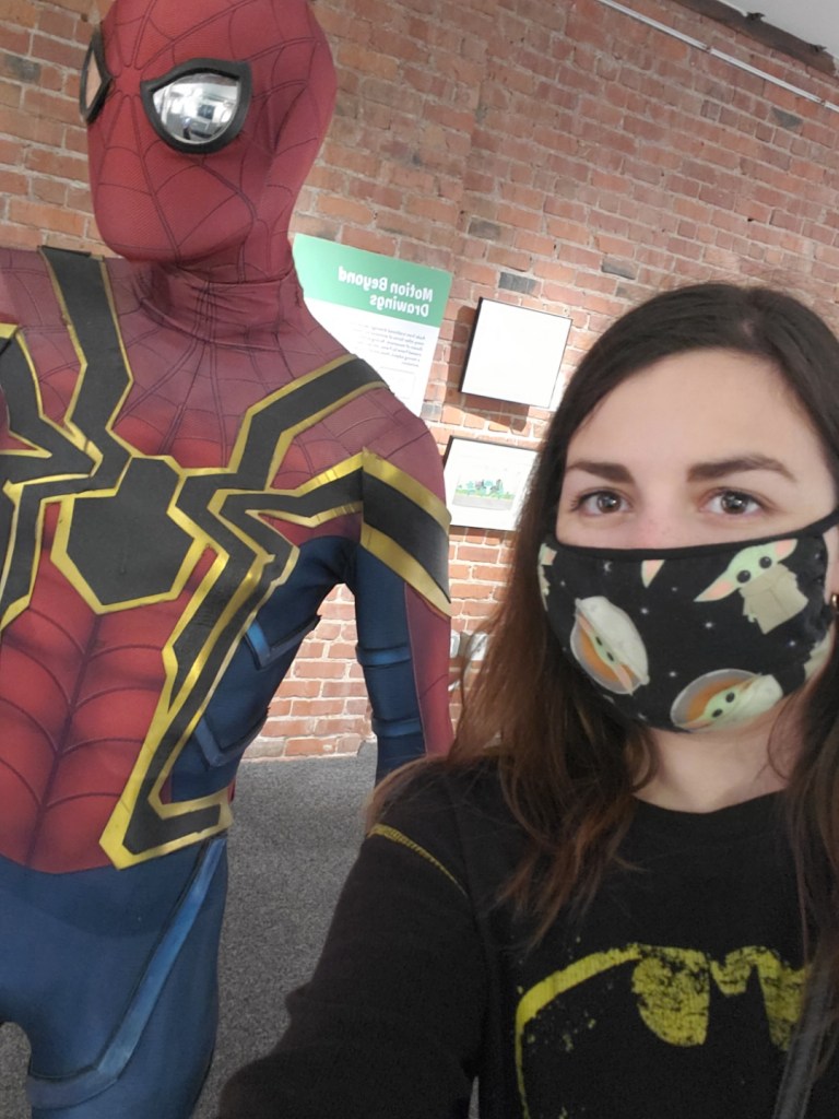 Image is a photo of me wearing a Baby Yoga mask. On my left is a life like statue of Spider-Man. 
