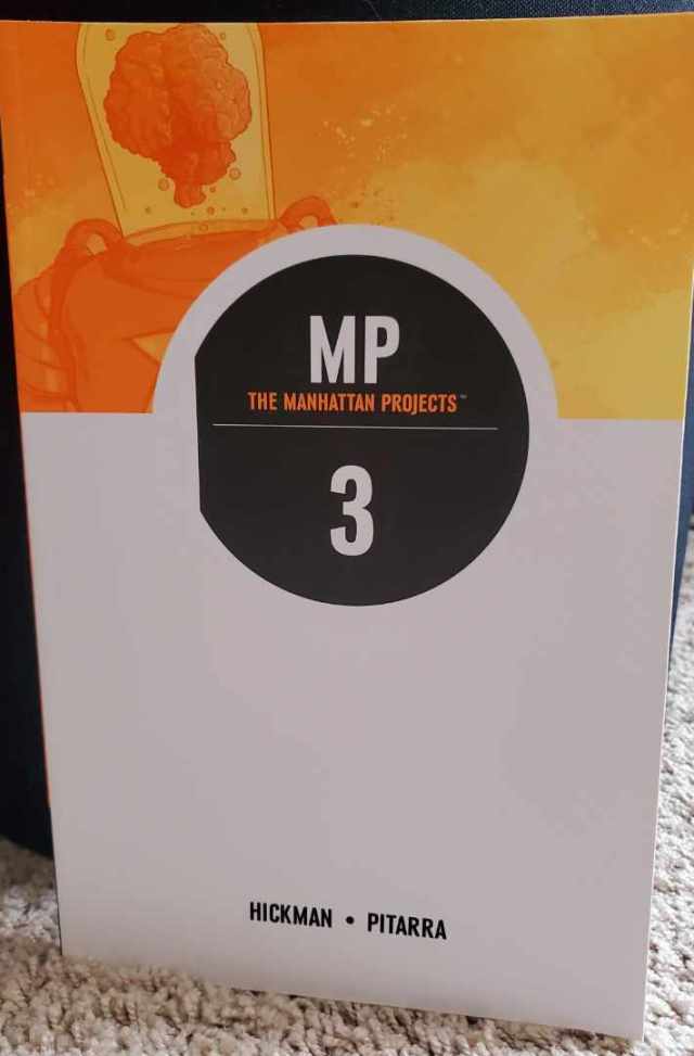 Image is a photo of The Manhattan Projects Volume #3. It's a white, black, and yellow graphic novel. The first third of the graphic novel is in yellow and it shows a mech with a glass tube. In the glass tube is a brain. There's a black circle with MP The Manhattan Projects and a white 3 in the middle. The rest of the graphic novel is white.