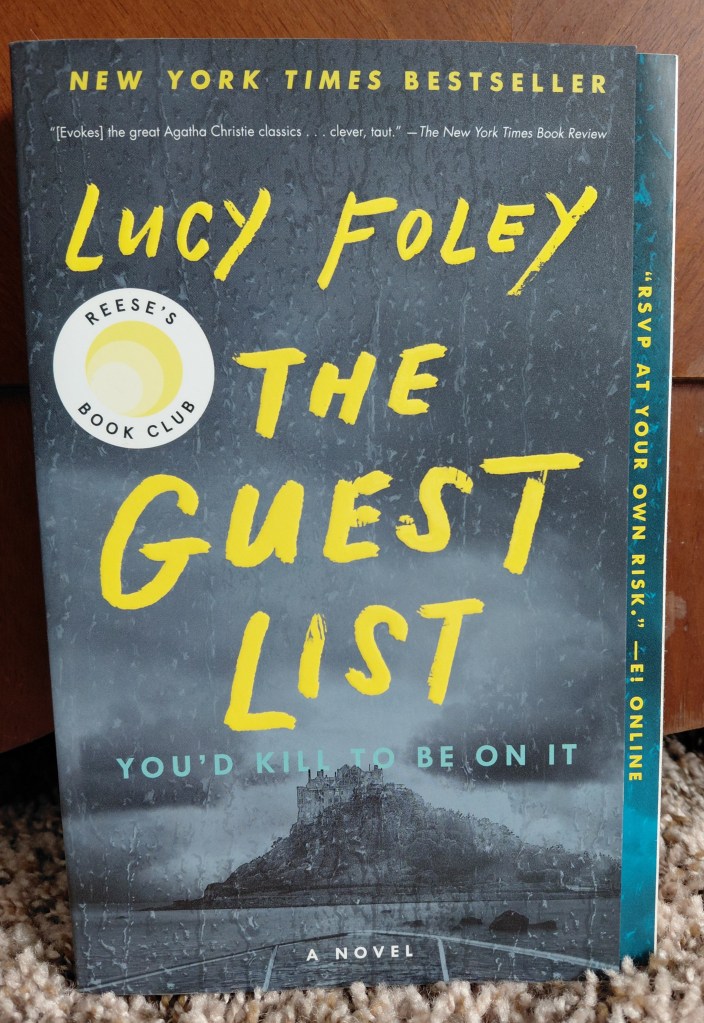 Image is a book cover for the book, The Guest List by Lucy Foley. It's a gray book with a rocky hill in the background. There's a mansion on the hill. The Guest list is in yellow chunky font. In smaller letters it says "You'd Kill To Be On It"