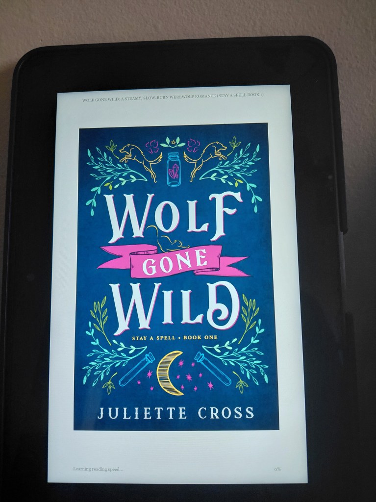 Image is a photo of the cover of Wolf Gone Wild on my Kindle. This photo was taken by me. It shows a black Kindle, a white background and the book cover. 

The book cover is a deep blue with light blue, green and yellow leaves. There's a potion bottle at the top center of the book. The font says Wolf Gone Wild Stay A Spell Book One by Juliette Cross. 