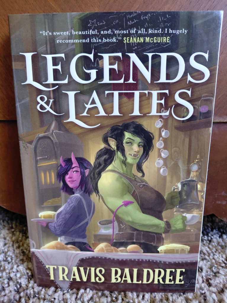 Image is a book cover for the book Legends & Lattes. There's a green orc with her hair pulled up in a pony tail. To the left is a bright pink woman with two horns on her forehead. 