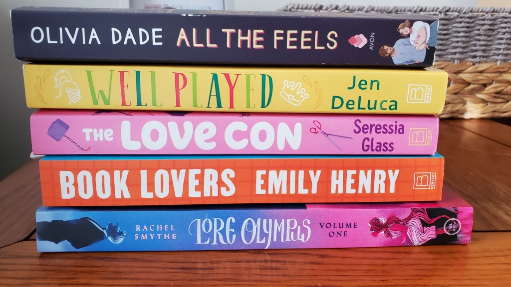 [Image shows a stack of five books. These are the book titles from top to bottom. "Olivia Dade All The Feels" "Well Played Jen DeLuca" "The Love Con Seressia Glass" "Book Lovers Emily Henry" "Lore Olympus Rachel Smythe Volume One" 