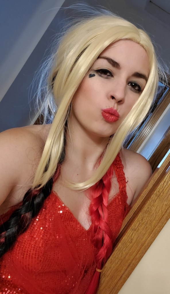 [Image is a woman posing in a red dress, blonde wig, and red lips]