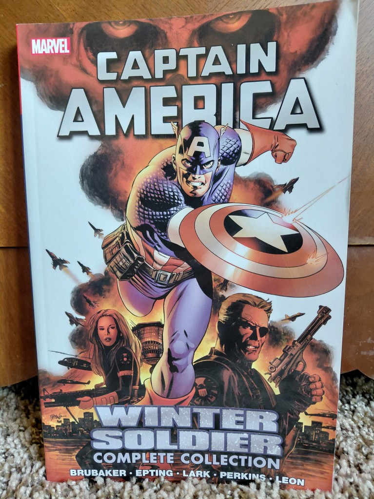 Image is a photo of a graphic novel cover for Captain America Winter Soldier Complete Collection. It shows Captain America front and center with his shield held on his right arm. Beneath him is a SHIELD agent and Nick Fury to his right. 