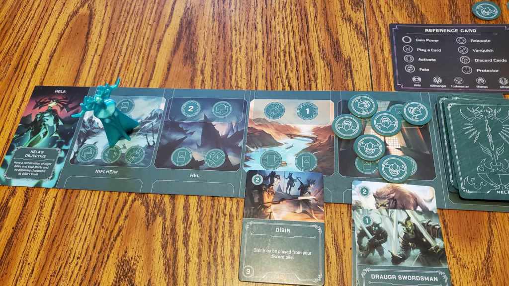 [Image features a game board. It's a green game board with four locations. There's a deck at the right and a character description on the left. It features Hela. Hela has a green outfit that glows on the left.]