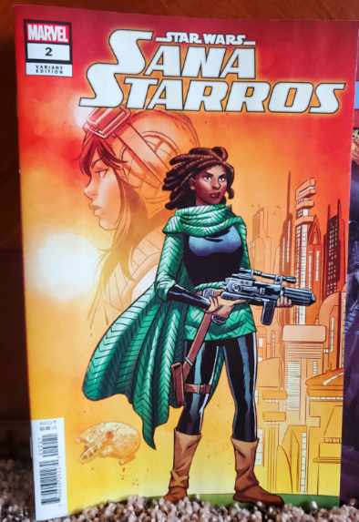 [Image is a comic cover. It shows a woman holding a blaster with a green robe / cape. In the background, it shows a woman wearing a pilot helmet.]