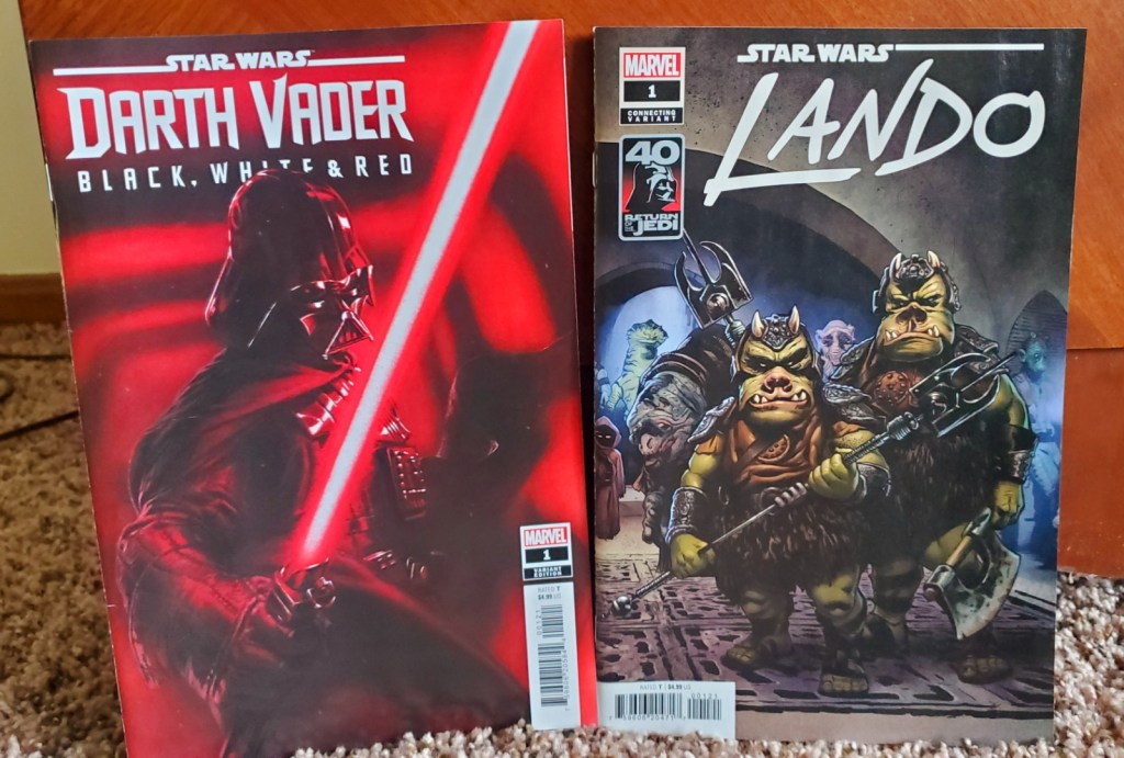 [Image is of two comics. One is Darth Vader, Black, White, and Red. It's showing Darth Vader with his red light saber in a shadowy hallway. The other comic on the right is Star Wars Lando. It shows some of the guards in Hutt's palace looking menacingly at the reader]