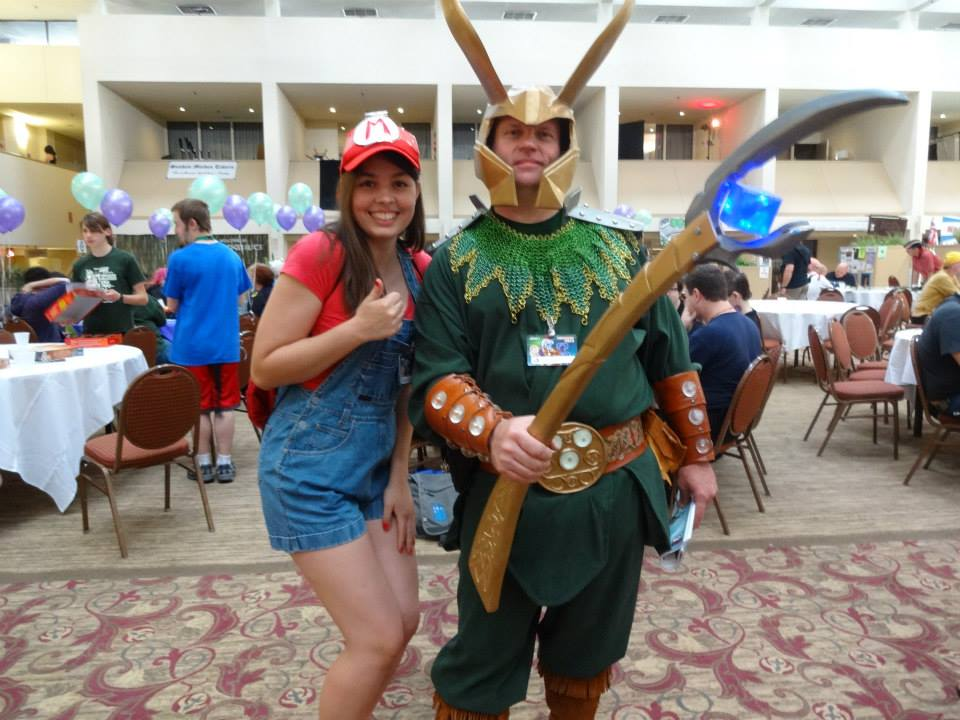 Image is of me and a person in cosplay. I'm dressed as Mario with the blue overalls and red shirt. The person next to me is dressed in green as Loki with the Staff]