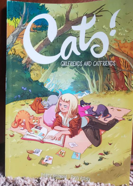 [Image is a graphic novel over of a woman sitting on a blanket and having a picnic. The are five cats lounging beside her. The graphic novel says Cats! Girlfriends and Catfriends on it]