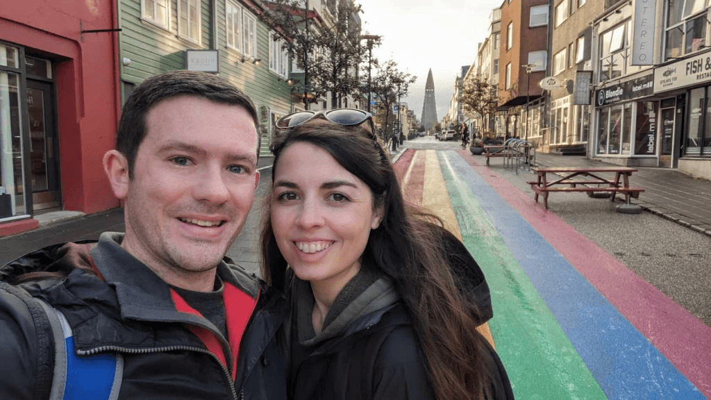 Photo is of me and my husband in Iceland. The road has a rainbow and there's a big church off in the distance. 