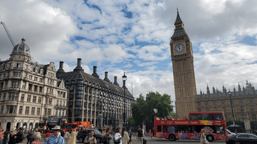 Photo is of Big Ben. There's a red decker tour bus on the road passing by.
