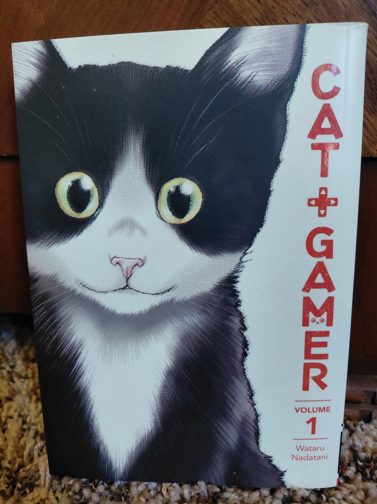Image is a photo for th manga, Cat Gamer. It shows a cute, black and white kitty. To the right, it has Cat Gamer with an arrow keypad between Cat and Gamer. The title is listeed vertically in red.