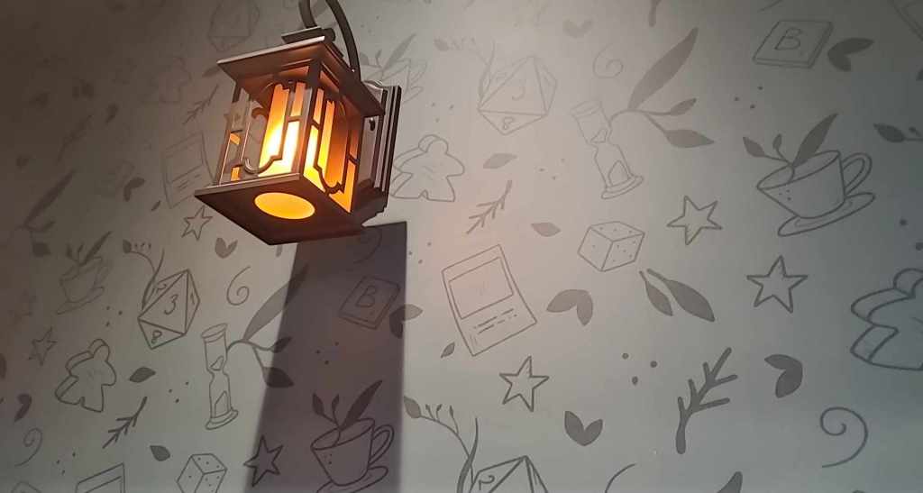 Image shows wall paper with dice, tea, game pieces, and an hour glass on it. There's a lantern that looks like a lantern hanging off an old building