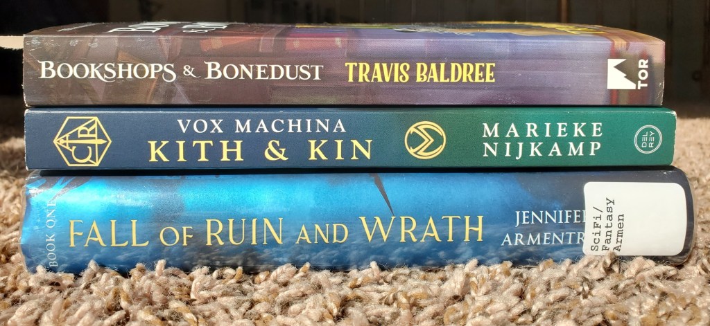Image features three books stacked vertically on top of each other. The first book is Bookshops & Bonedust by Travis Baldree, the second book is Vox Machina Kith & Kin by Marieke Nijkamp and the third book is Fall of Ruin and Wrath by Jennifer Armentrout.