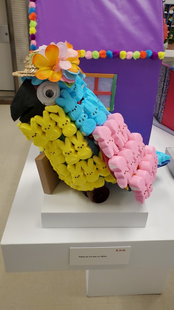 Image is a parrot, but lining the parrot's back are blue, pink, and yellow peeps.