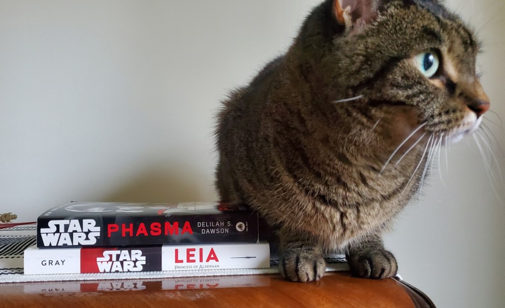Image is a stack of two books, the first is Phasma by Delilah S. Dawson and the second is Leia Princess of Alderaan. To the right, is a tabby cat that insisted on being in the photo. She's staring out the window. 