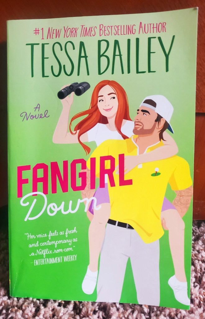 Image is a book cover for Fangirl Down by Tessa Bailey. The book cover has a red-haired woman on a piggy back ride with a man who's a pro-golfer.