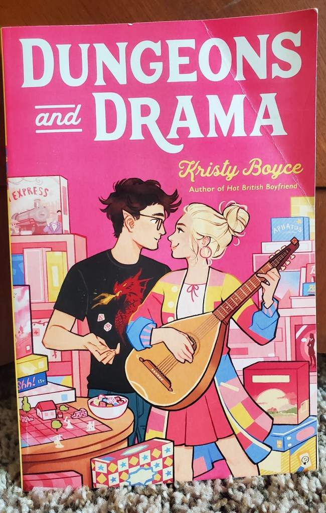 Image is a book cover for Dungeons and Drama by Kristy Boyce. It shows a boy and a girl staring at each other. The boy is juggling dice, the girl is playing a guitar. There are board games in the background. 