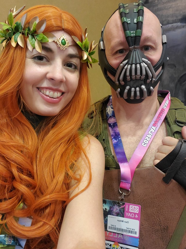 Image is a selfie of me as Keyleth in a bright orange wig and my friend who is cosplaying as Bane from Batman. 