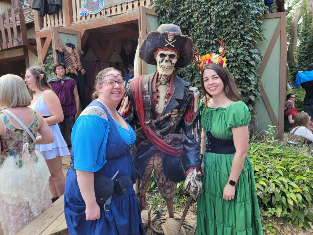 Image is a photo of me and a friend at the Renaissance Festival. She's dressed up in blue, I'm in green. In the middle is a skeletal pirate. 